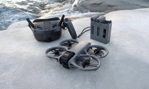 DJI drone with propellers, controller, carrying case, and charging hub displayed on snow near ocean waves