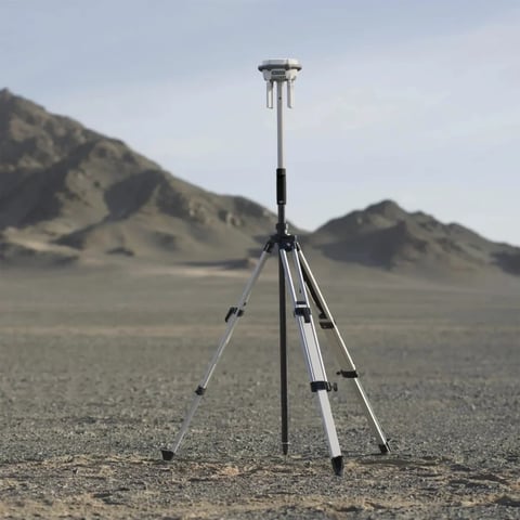 Surveying equipment tripod with GPS antenna set up on barren desert landscape with rocky hills in background
